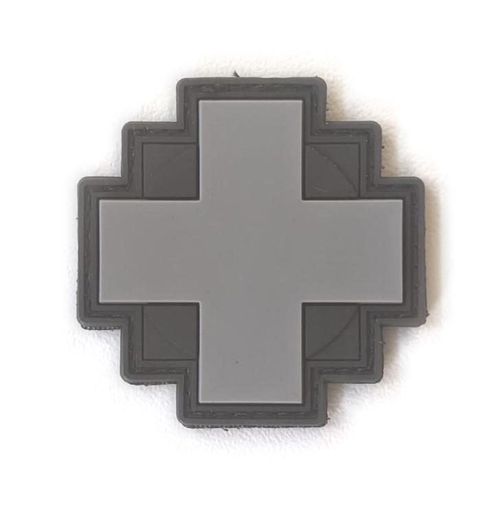 3-D Rubber Patch Medic in Kreuzform mit matter, flexibler Oberfläche und kontrastierendem, dunklem Rand auf weißer Wand befestigt.