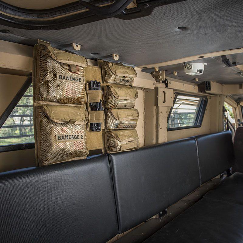 Mehrere schwarze Netzpouches mit Bandagen und medizinischen Utensilien befestigen sich am Chinook Medical Panel im Innenraum eines gepanzerten Fahrzeugs.