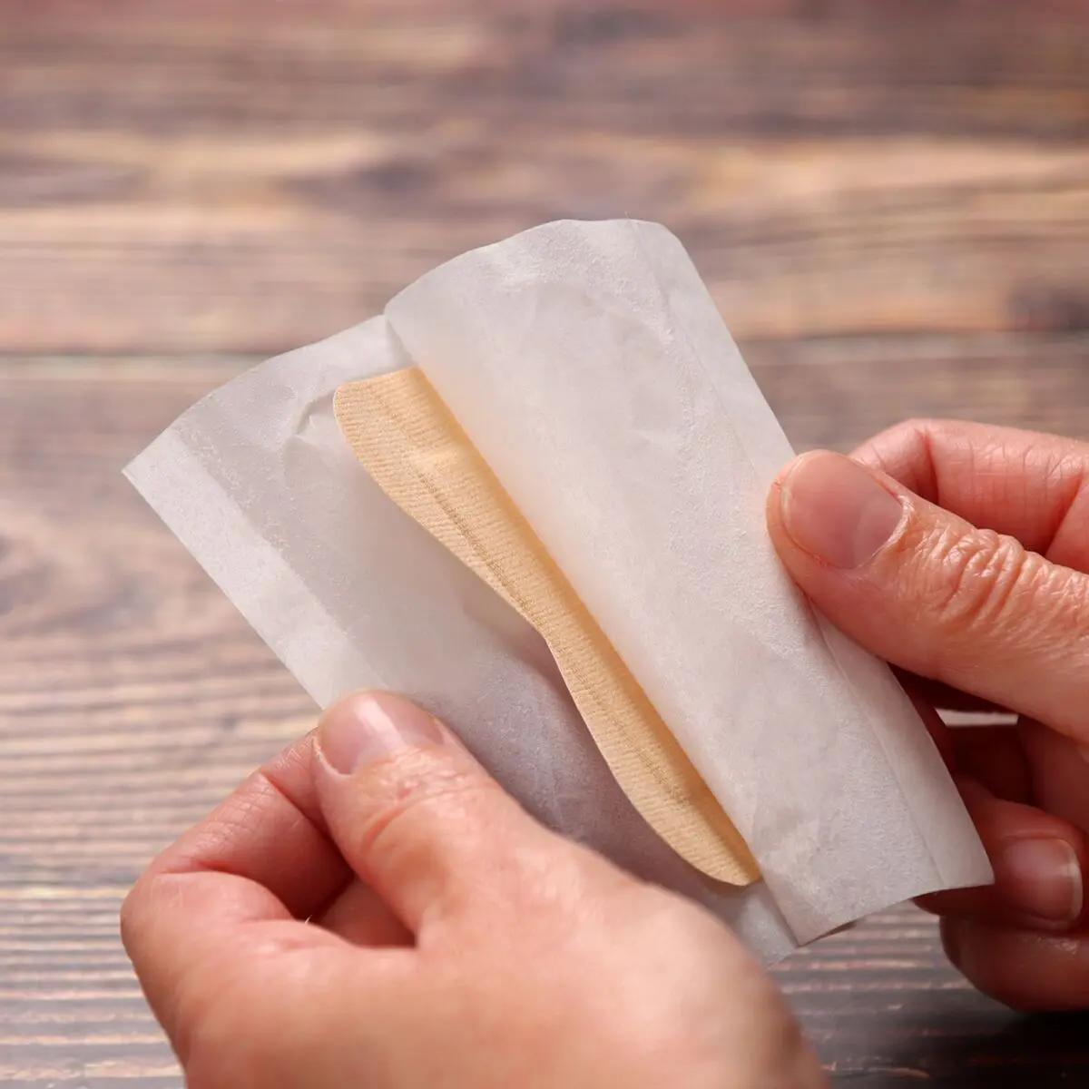 Alt-Text: Zwei Hände halten ein Fingerkuppenpflaster Weroplast® MasterTex, das aus anpassungsfähigem, textilem Gewebe besteht und in weißer Umverpackung steckt.