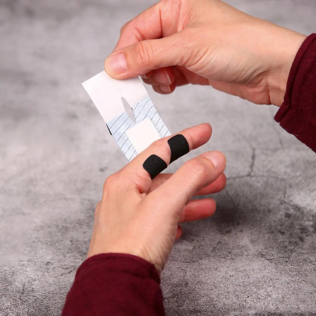 Eine Person mit rotem Shirt legt einen Weroplast® PowerTex Pflaster - Mini Mix Streifen mit extra starker Klebkraft auf den Mittelfinger.