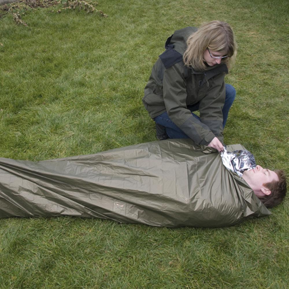 Eine Frau legt einem Mann in einem Schlafsack die silberfarbene, wärmereflektierende WERO MED-X® Rettungsdecke mit schwarzem Mittelteil um.