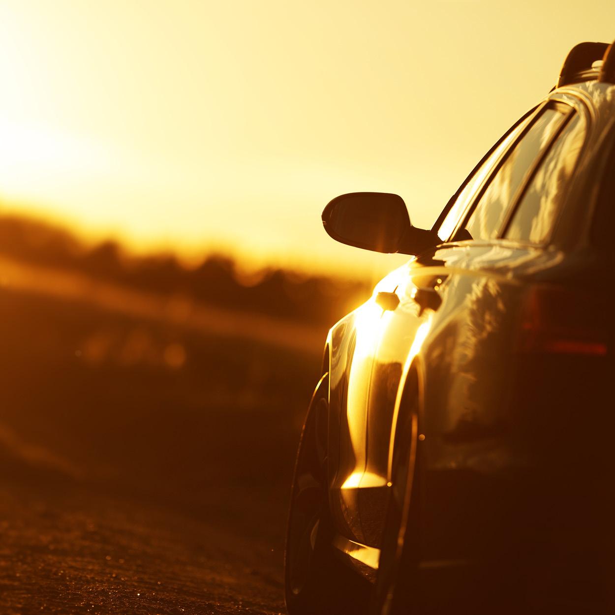 Ein Auto fährt dem Sonnenuntergang entgegen. Die Sonne spiegelt sich im Lack.