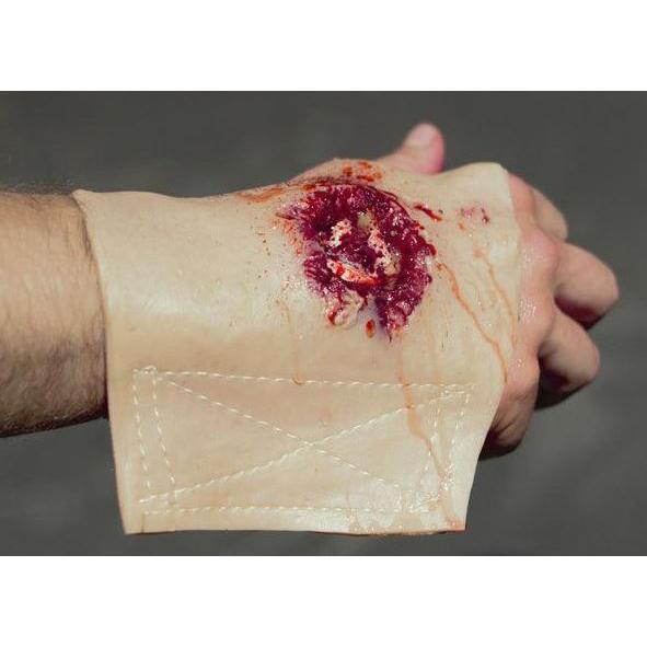 Eine rechte menschliche Hand hält die Techline Moulage Schusswunde Hand rechts, die eine realistische Schussverletzung mit sichtbarem Gewebe simuliert.