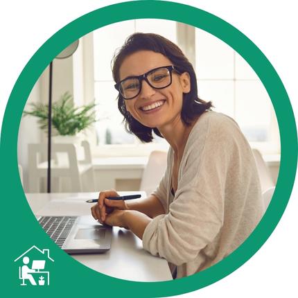 Eine Frau mit dunklem Haar arbeitet am silbernen Laptop, trägt einen beigen Pullover und hält einen schwarzen Stift in der Hand.