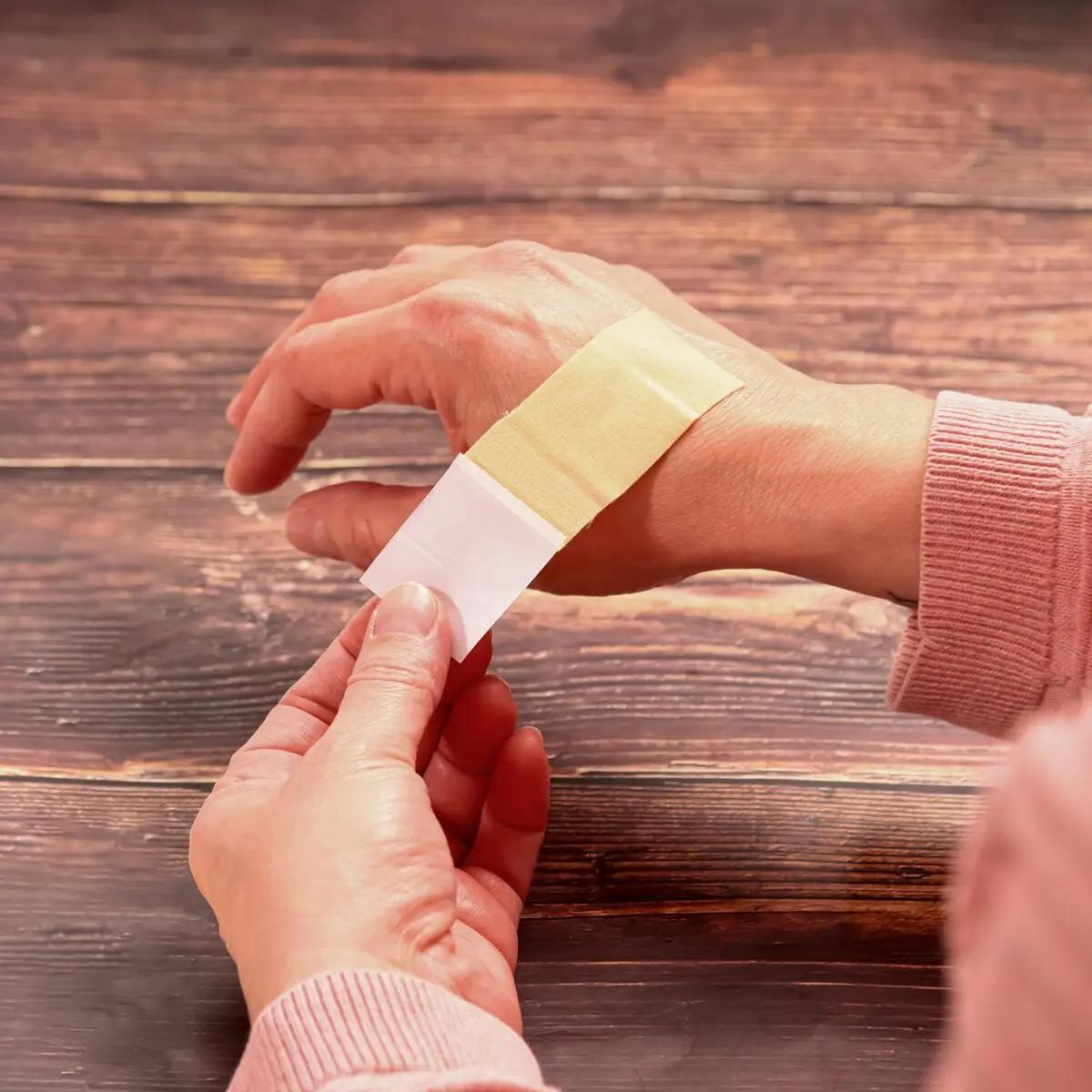 Ein Weroplast® MasterTex Wundschnellverband wird mit den Händen zugeschnitten und als flexibles, hautfarbenes Pflaster aufgetragen.
