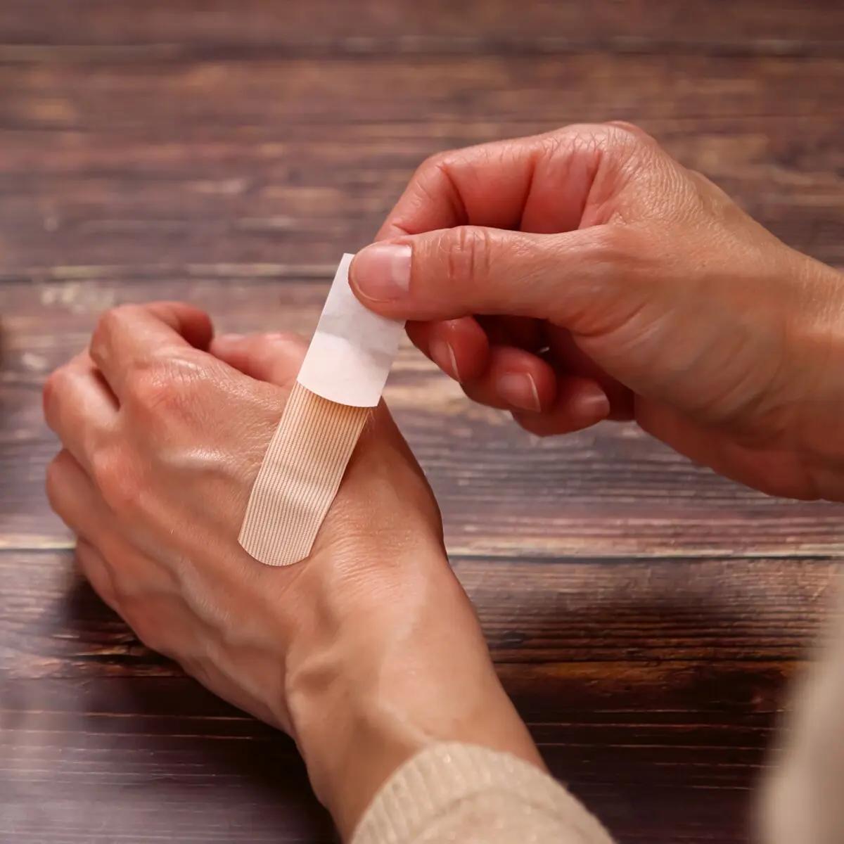 Zwei Hände mit hellem Teint halten ein teilweise gelöstes, beiges Weroplast® AquaFlex Pflaster - Mini Mix, das wasserdicht und flexibel ist.