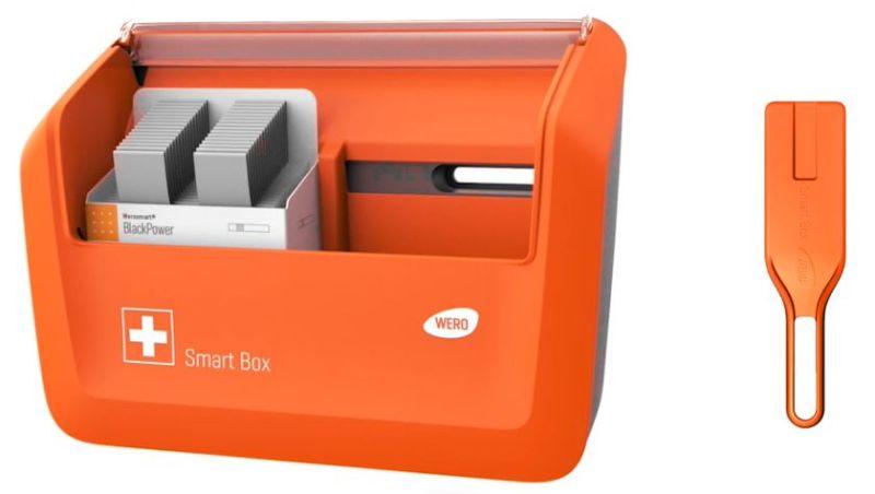 Orangefarbene WERO Smart Box mit Sichtfenster und Kartenschächten, weißem "Smart Box"-Label, rotem Kreuz und separatem Entnahmewerkzeug.