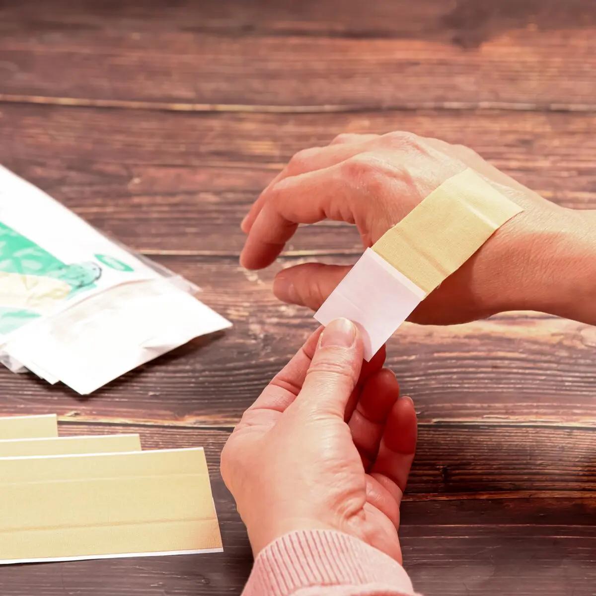 Zwei Hände kleben einen Wundschnellverband Weroplast® MasterTex aus beigem, anpassungsfähigem Textilgewebe vorsichtig auf ein Handgelenk.