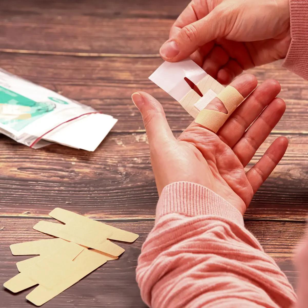 Eine Hand in rosa Shirt fixiert mit einem Fingergelenkpflaster Weroplast® MasterTex ein beiges, flexibles Pflaster mit Loch an einem Finger.