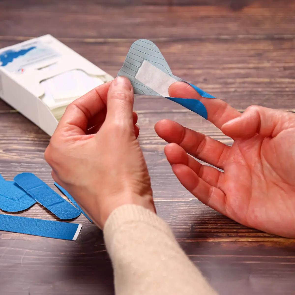 Eine Person legt ein blau-weiß gestreiftes Pflaster aus dem Pflasterset Weroplast® PowerDetect - Mix DIN 13157 mit robustem, detektierbarem Gewebe um den Finger.