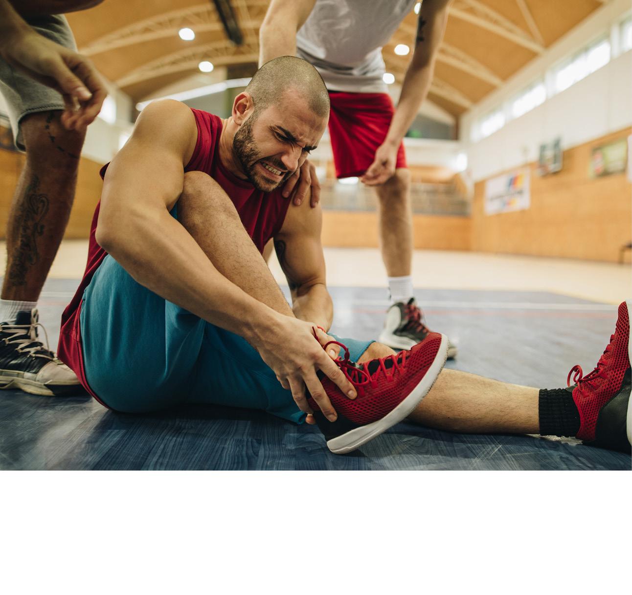 Ein Mann stützt mit schmerzverzerrtem Gesicht seinen Fuß, während er auf dem Boden sitzt.
