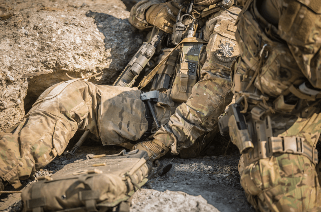 Zwei Soldaten sitzen am Boden. Neben der Uniform tragen Sie auch Ausrüstung bei sich, wie z.B. ein Tourniquet.