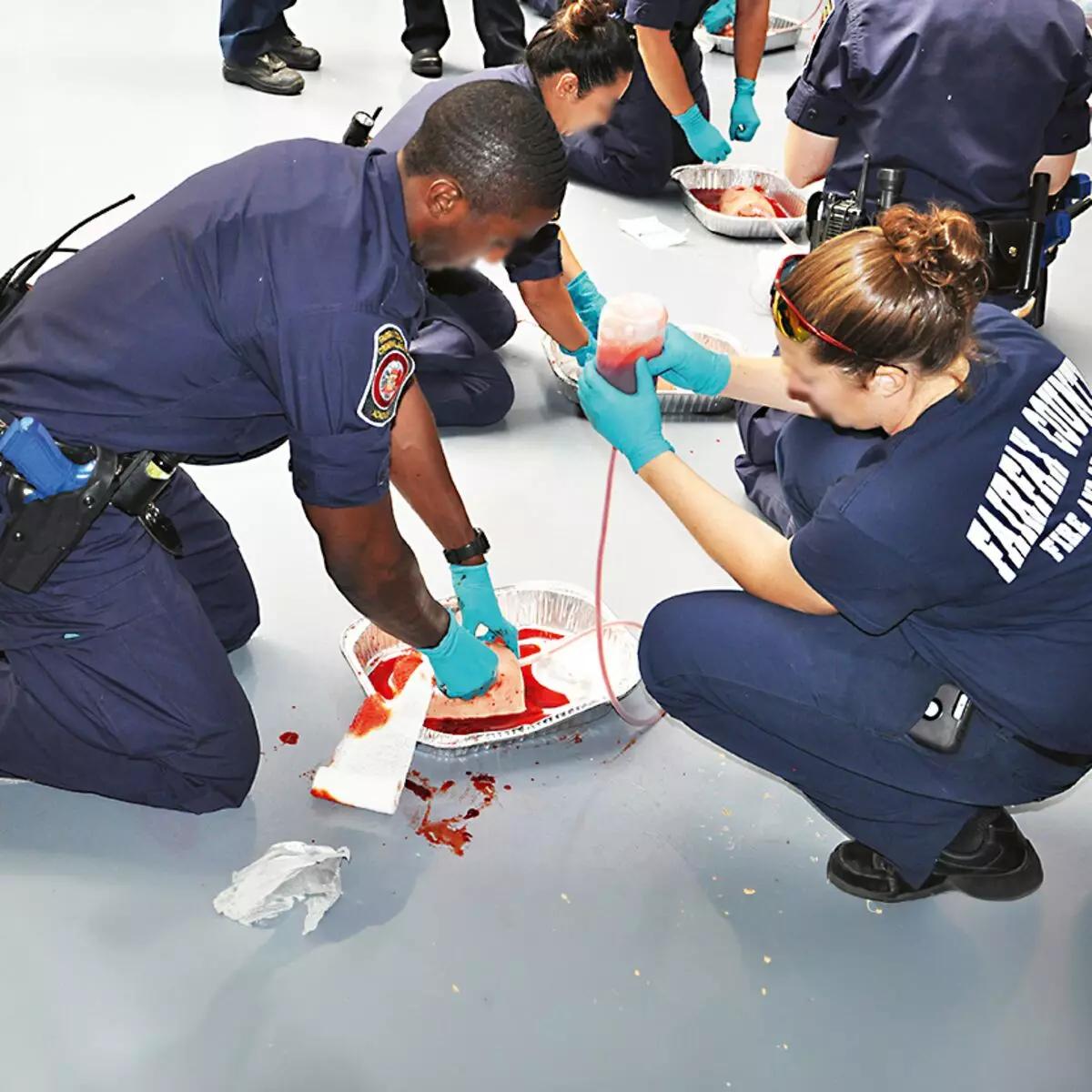 Mehrere Polizisten trainieren mit dem TrueClot® Wound Packing Trainingssystem Schnittwunde an einer Metallwanne mit künstlichem Blut und weißer Gaze.