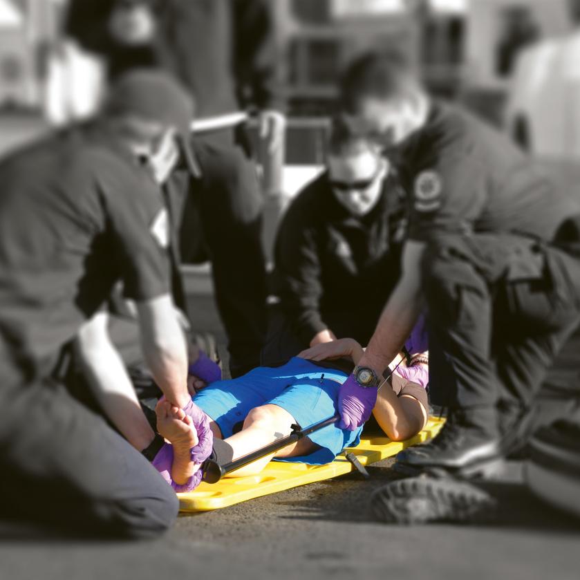 Mehrere Einsatzkräfte stabilisieren eine Person mit erhobenen Beinen, fixiert an einer Slishman Traction Splint (STS) auf einer gelben Trage, bei der Anwendung im Notfalleinsatz.