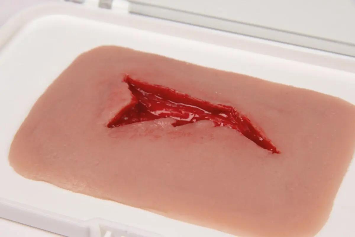 Rechteckige Erler-Zimmer Woundmoulage Risswunde mit unregelmäßigem Rand und tiefroter Wunde auf hellbeigem, leicht strukturiertem Material in weißer Schale.