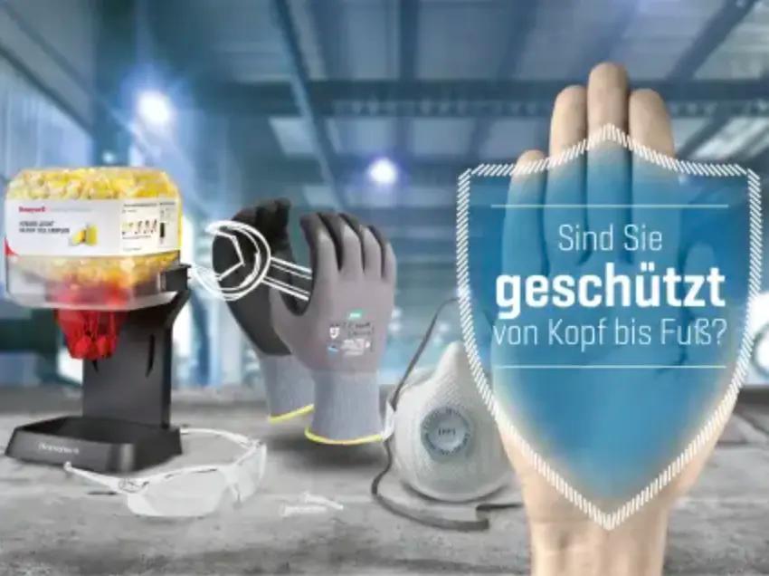 Verschiedene Arbeitsschutzartikel wie graue Handschuhe, Schutzbrille, Atemschutzmaske, Sicherheitsnadeln und Werkzeug auf einem Industrietisch.