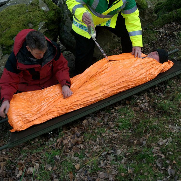 Eine Person liegt in einer Blizzard - Orange, Decke auf einer Trage, wird notfallmedizinisch betreut und vor Auskühlung geschützt.