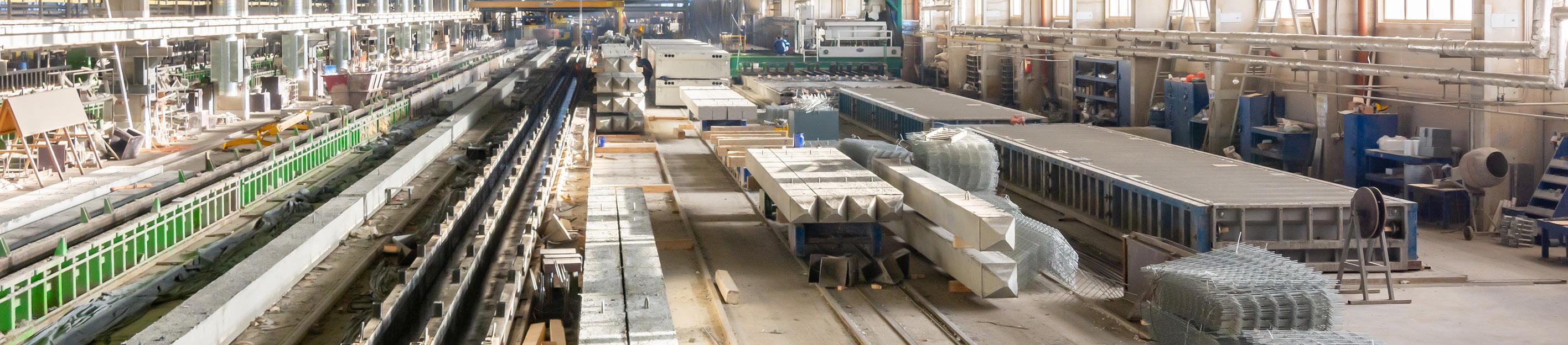 Innenansicht einer Fabrikhalle mit mehreren Schienen, darauf ein weißer Güterwagon und verteilt stehende Metallcontainer sowie Industrieanlagen.