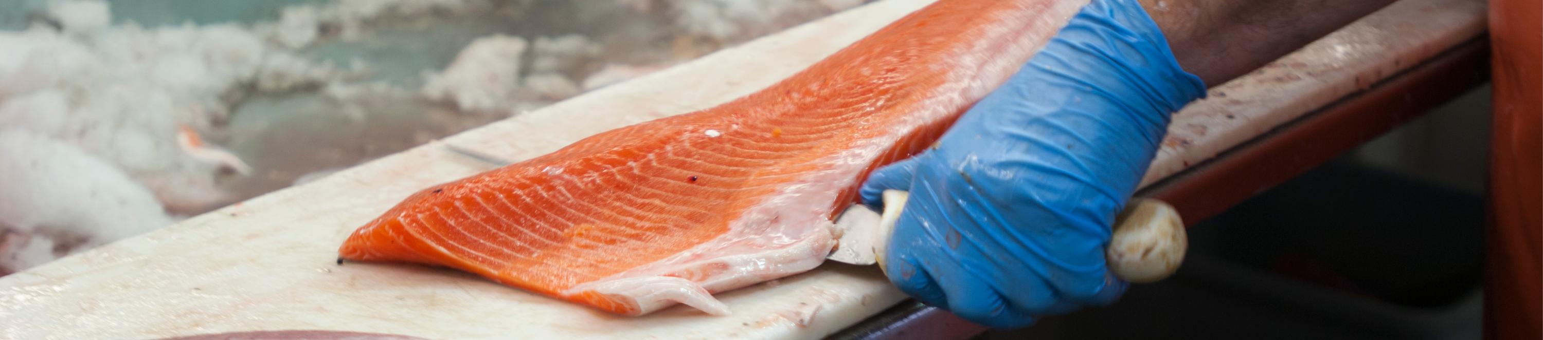 Eine Person schneidet ein großes Stück Lachs mit einem Messer.