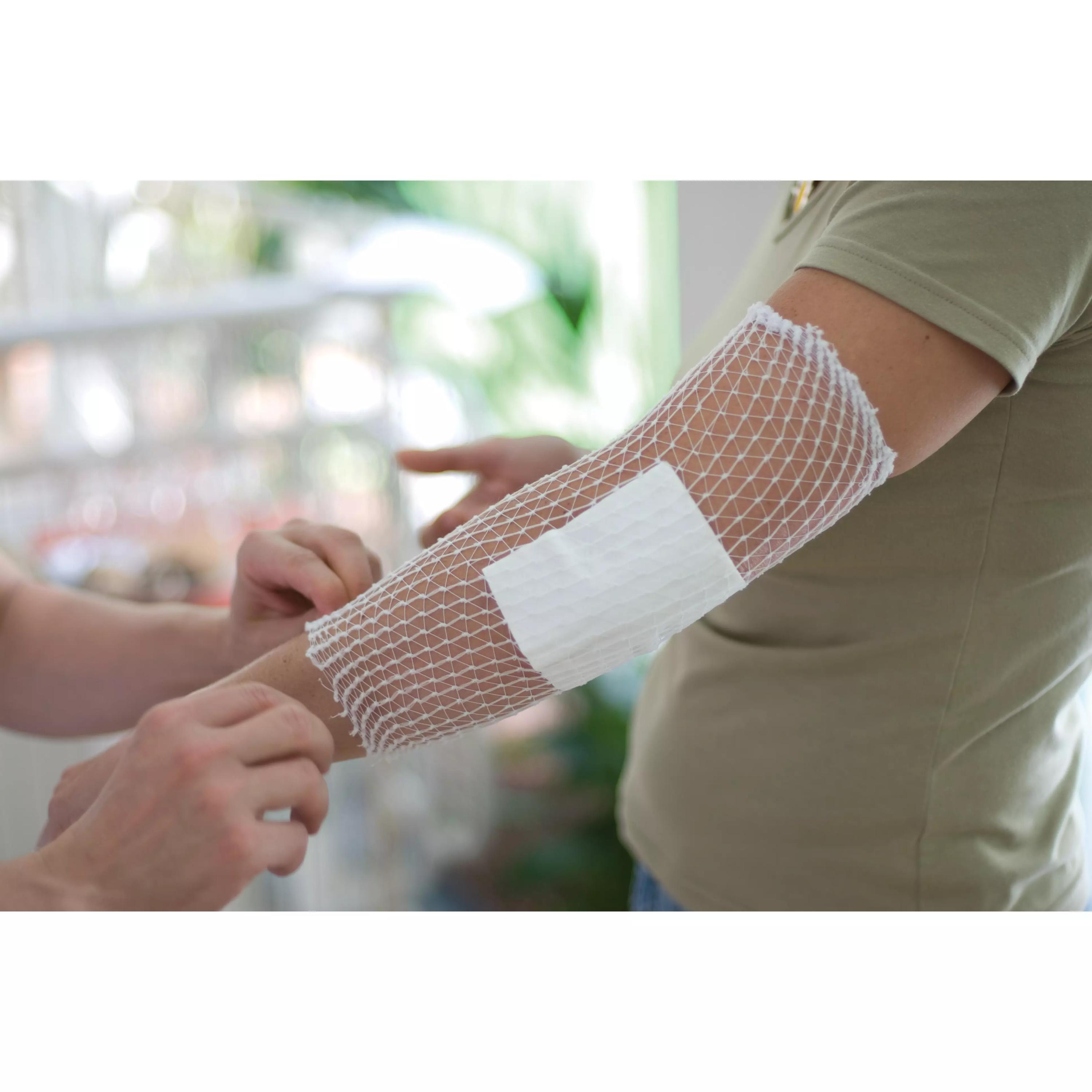 Eine Person trägt am Arm einen weißen Weronet® Netzverband, der mit hoher Flexibilität zur schnellen Fixierung einer Wundauflage angebracht wird.