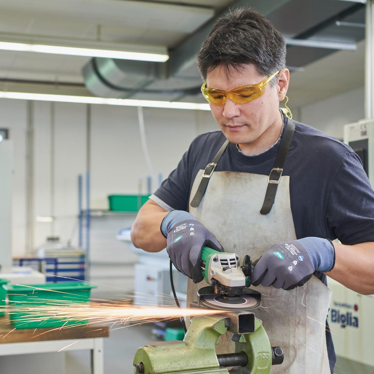 Ein Mann flext an einem Metallstück. Dabei trägt er eine Schutzbrille zum Augenschutz.