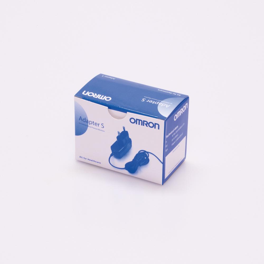 Weiße Verpackung vom Netzteil für Blutdruckmessgerät OMRON RS4 und M400 mit blauem Aufdruck und Abbildung des Adapters sowie Kabel auf der Vorderseite.
