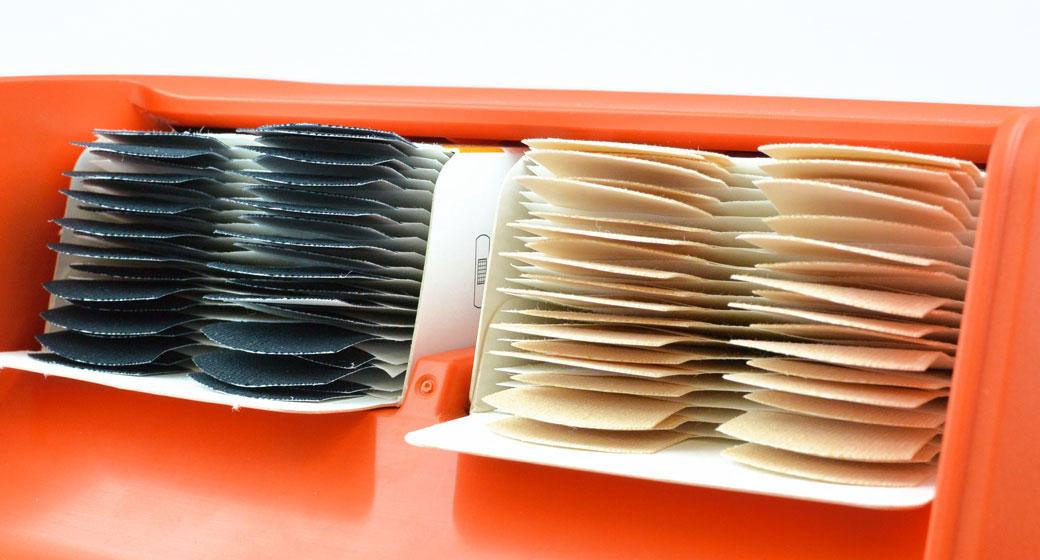 Roter Kunststoffbehälter mit zwei Fächern, befüllt mit beige- und schwarzgrauen elastischen, gewebten Bändern.