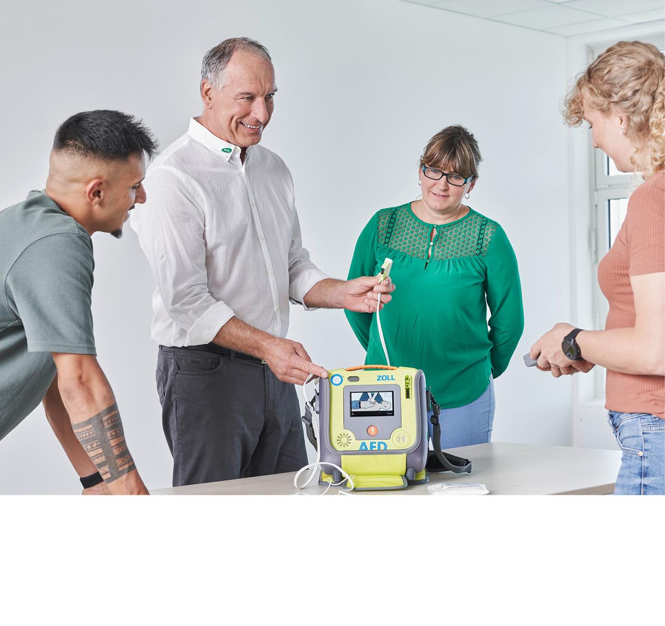 Ein WERO-Mitarbeiter erklärt mehreren Kunden die Nutzung eines AED-Defibrillators.