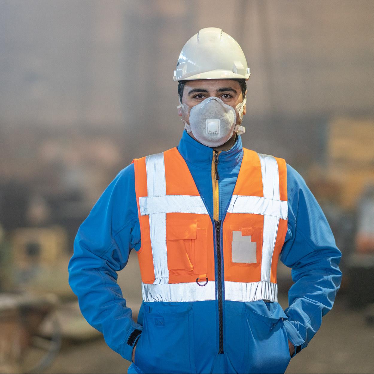 Ein Mann vom Kopf bis zur Hüfte. Er trägt einen Schutzhelm sowie Schutzkleidung und eine Atemmaske. 
