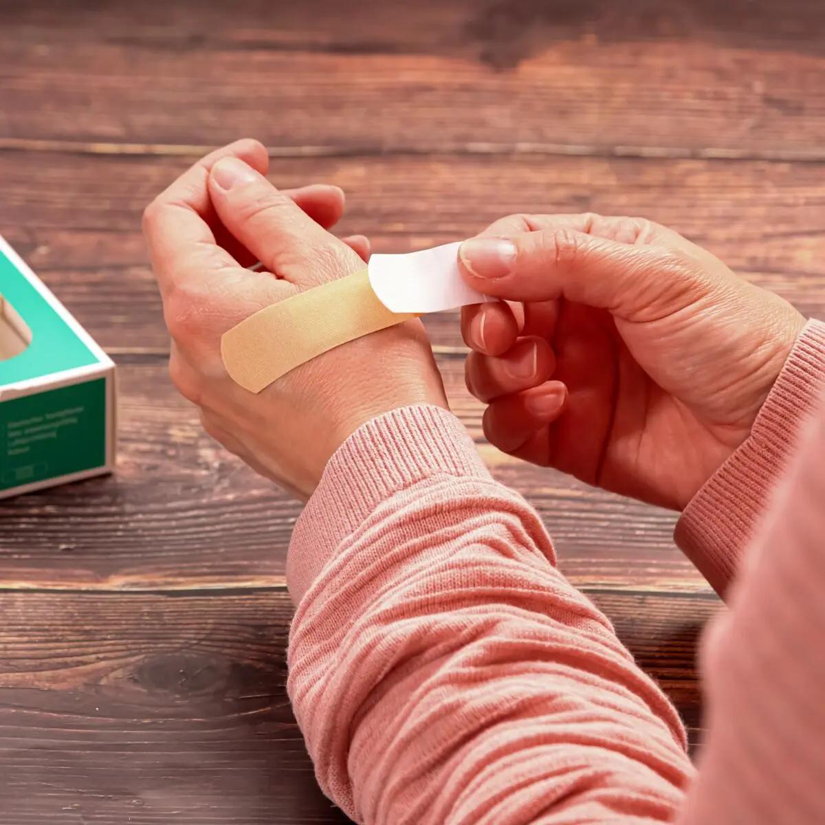 Eine Hand legt einen hautfarbenen Pflasterstrip Weroplast® MasterTex mit anpassungsfähigem, textilem Gewebe sorgsam auf ein Handgelenk an.