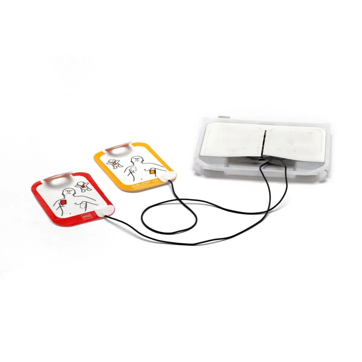 Zwei unterschiedlich farbige LIFEPAK CR2 Trainingselektrodenablagen mit illustrierten Symbolen und schwarzem Kabel liegen nebeneinander vor einer offenen weißen Box.