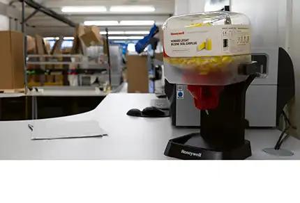 Honeywell Ohrstöpselspender aus transparentem Kunststoff mit rotem Deckel, befüllt mit gelben und roten Gehörschutzstöpseln auf Werktisch