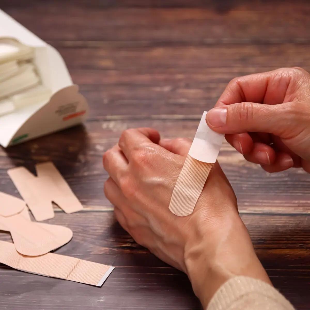 Eine Hand hält ein beigefarbenes Weroplast® AquaFlex Pflaster - Perfect Mix, das wasserdicht und flexibel auf die Haut am Handgelenk aufgebracht wird.