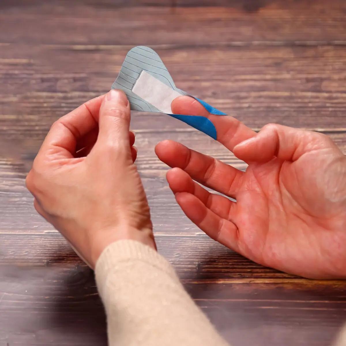 Zwei Hände halten ein blau-weißes Pflasterset Weroplast® PowerDetect, das dank detektierbarem, elastischem Gewebe und Aluminiumstreifen gut sichtbar ist.
