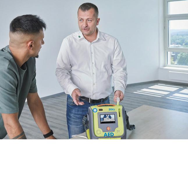 Ein Mann hält einen ZOLL AED Defibrillator, neben ihm steht eine zweite Person in legerer Kleidung in einem hellen Raum.