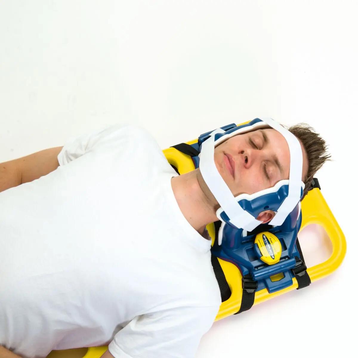 Eine Person liegt entspannt auf einem gelben Spineboard, der Kopf sicher mit der Kopffixierung für Spineboard aus abwaschbarem, latexfreiem HDPE fixiert.
