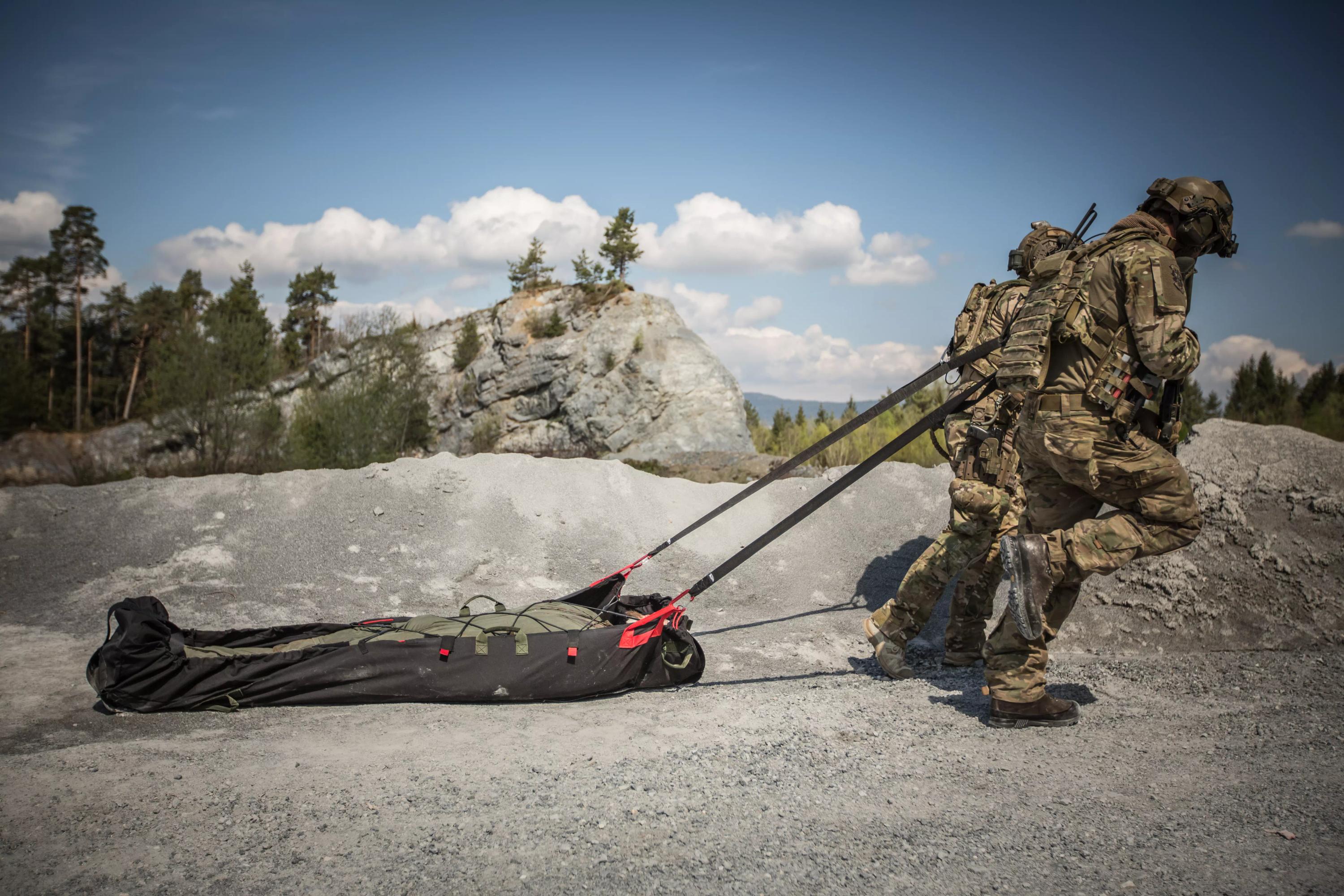 Zwei Soldaten in Tarnkleidung trainieren mit dem Xtract™ SR Module, einem kompakten Rettungsset, das auf dem Rücken getragen und auf rauem Gelände bewegt wird.