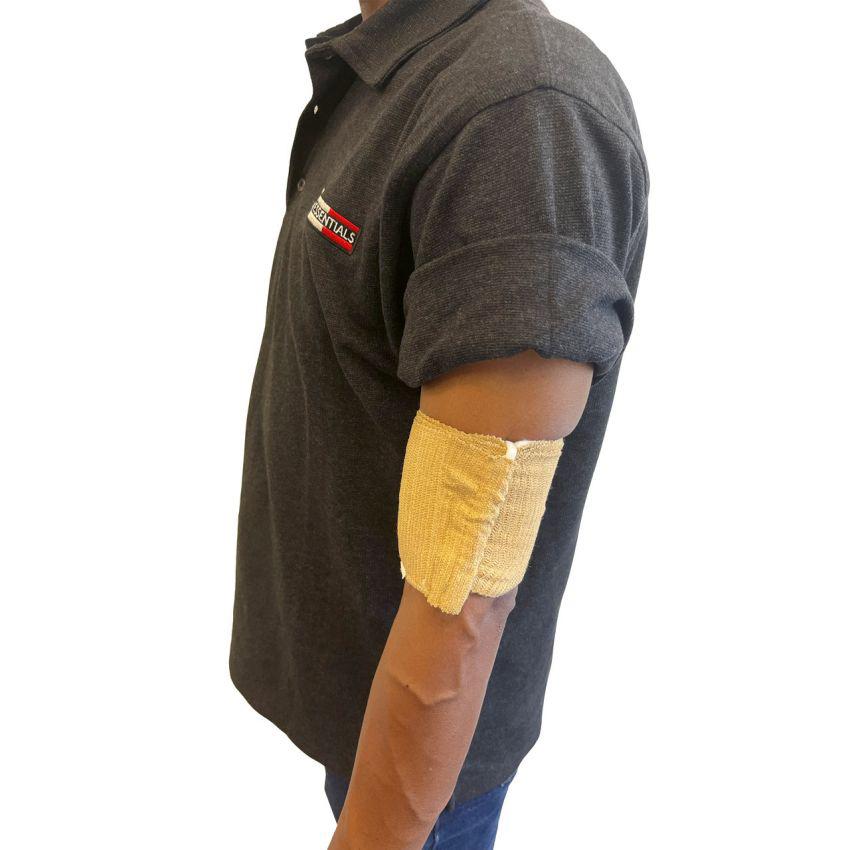 Eine Person trägt die Rescue Essentials® Mini Compression Bandage als beigen Verband mit sichtbarer Falte am Unterarm über einem dunkelgrauen Polo und blauen Jeans.