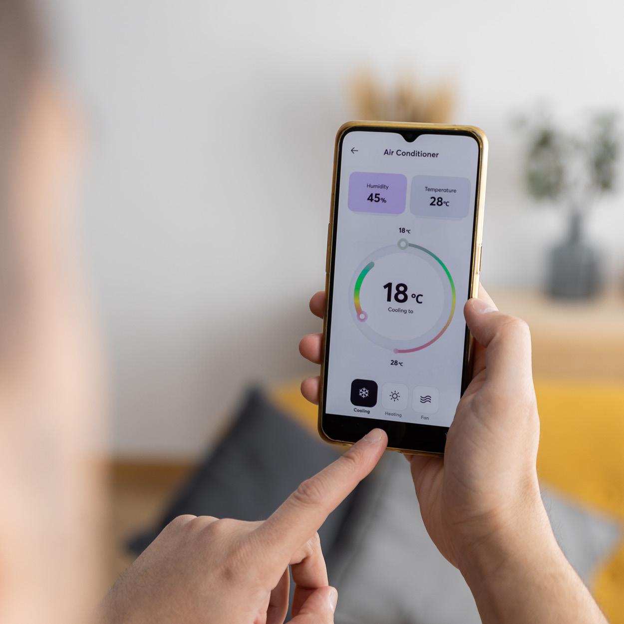 Zwei Hände bedienen ein Smartphone. Auf dem Smartphone ist die Bedieneinheit für eine Klimaanlage zu sehen.