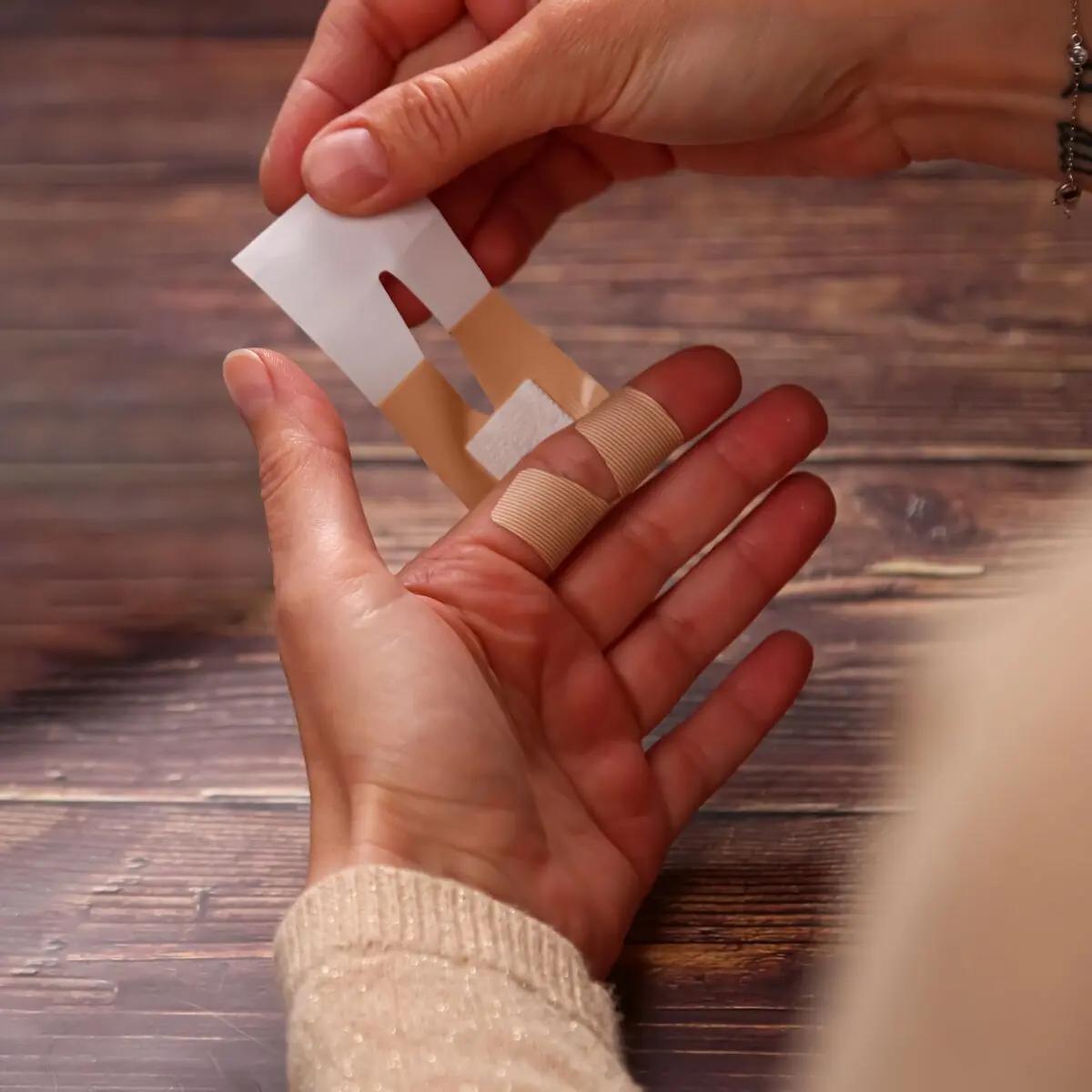 Eine Hand befestigt ein beigefarbenes Weroplast® AquaFlex Pflaster - Mini Mix auf einem Finger, ein weiteres wasserdichtes, flexibles Pflaster wird gehalten.