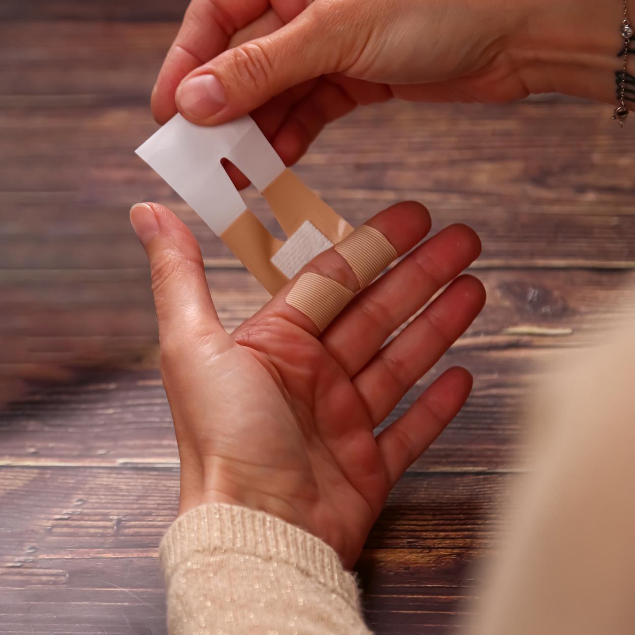 Eine Hand befestigt ein beigefarbenes Weroplast® AquaFlex Pflaster - Mini Mix auf einem Finger, ein weiteres wasserdichtes, flexibles Pflaster wird gehalten.