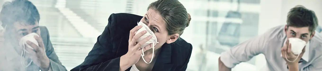 Mehrere Personen mit weißen Papiermasken sitzen an einem Besprechungstisch in einem modernen Büro mit großen Fenstern.