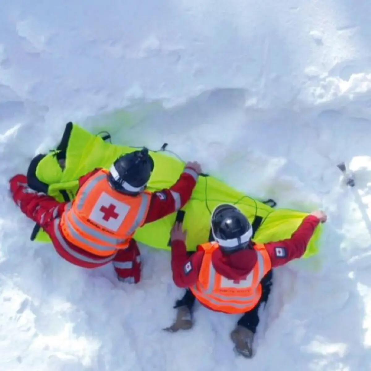 Zwei Personen heben gemeinsam den Thermosaver Hypothermic Rescue Bag - Grau mit wasserabweisender, winddichter Außenschicht und isolierender Faserfüllung im Schnee.