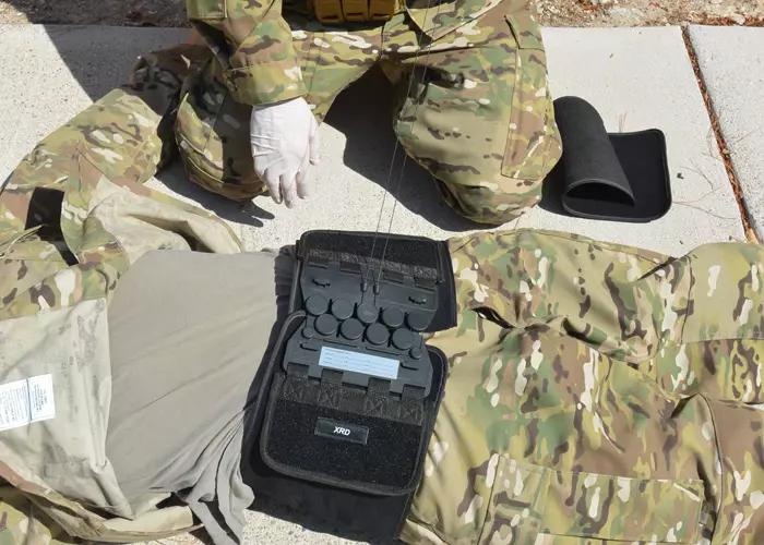 Eine Person in Tarnkleidung kniet am Boden und legt einen Arrow® T-POD™ - Schwarz an, der durch Seilzugsystem eine gleichmäßige, zirkuläre Kompression ermöglicht.