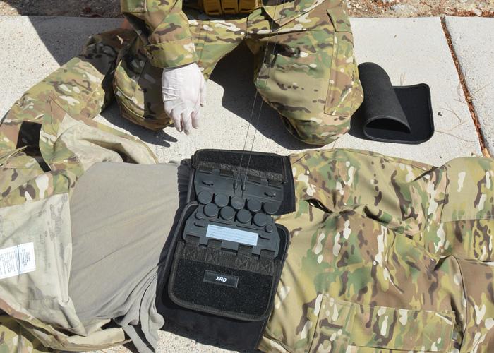 Eine Person in Tarnkleidung kniet am Boden und legt einen Arrow® T-POD™ - Schwarz an, der durch Seilzugsystem eine gleichmäßige, zirkuläre Kompression ermöglicht.