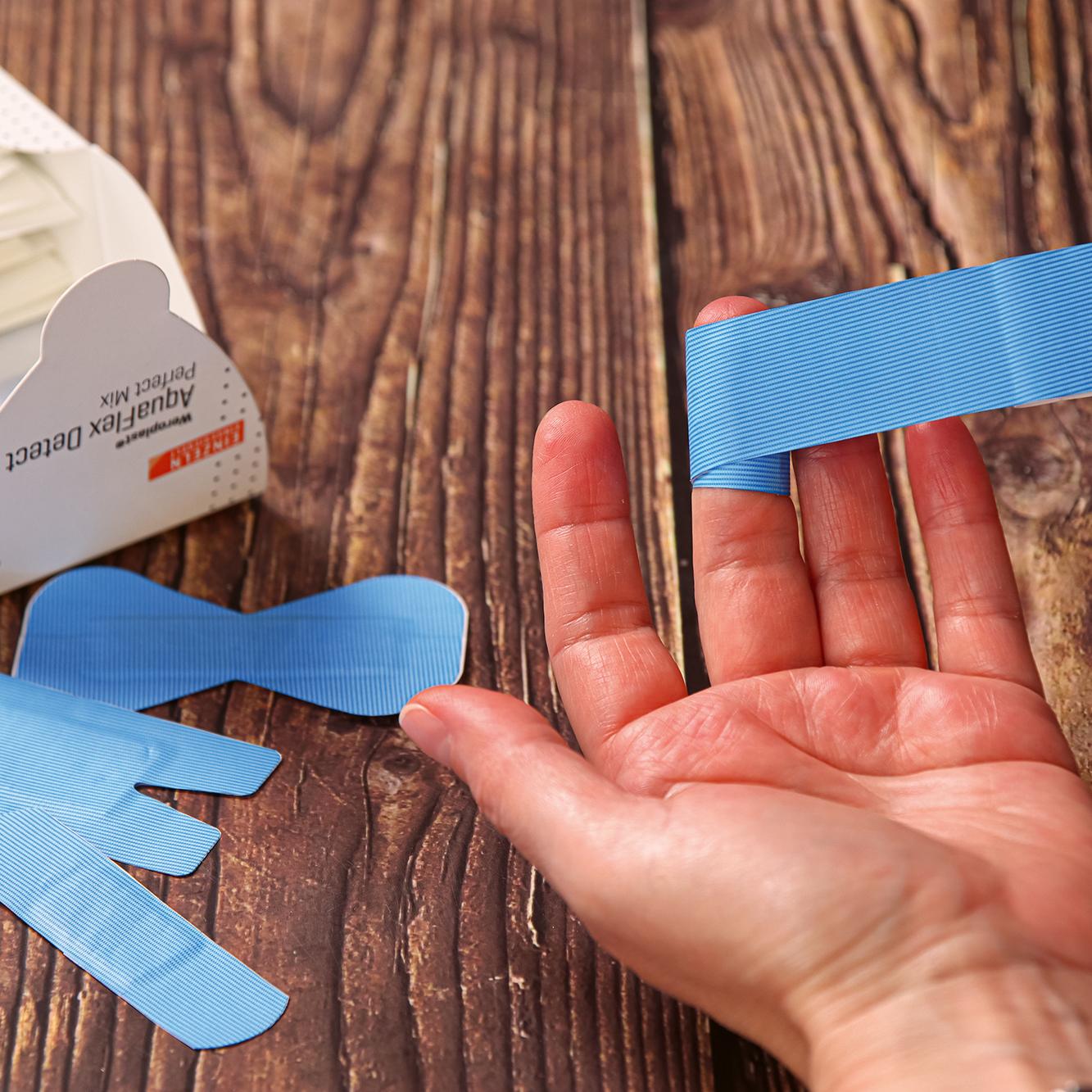 Eine Hand demonstriert die Anwendung eines blauen Pflastersets Weroplast® AquaFlex Detect - Perfect Mix, das elektromagnetisch und visuell detektierbar ist.