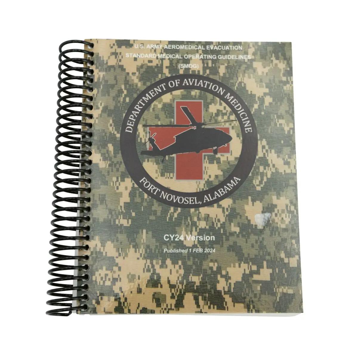 Ein spiralgebundenes Standard Medical Operations Guide CY 2024 Buch mit Camouflage-Muster und rotem Kreuz-Emblem auf dem Cover.