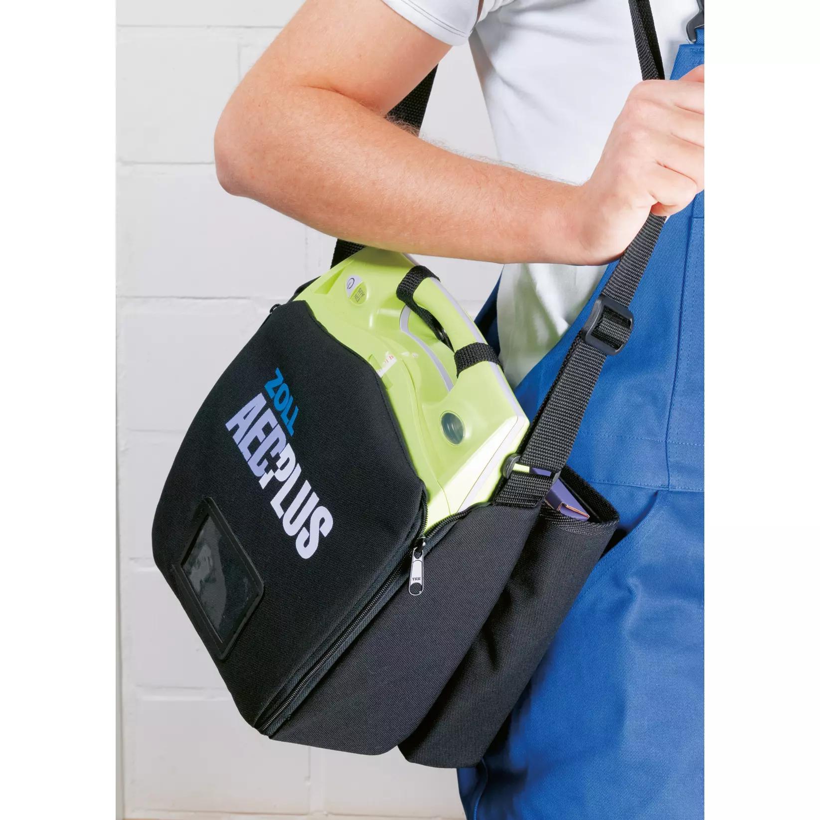 Eine Person trägt die ZOLL AED Plus Soft-Tasche, leer, über der Schulter und hält sie mit beiden Händen, der Defibrillator ist im Inneren gut gesichert.