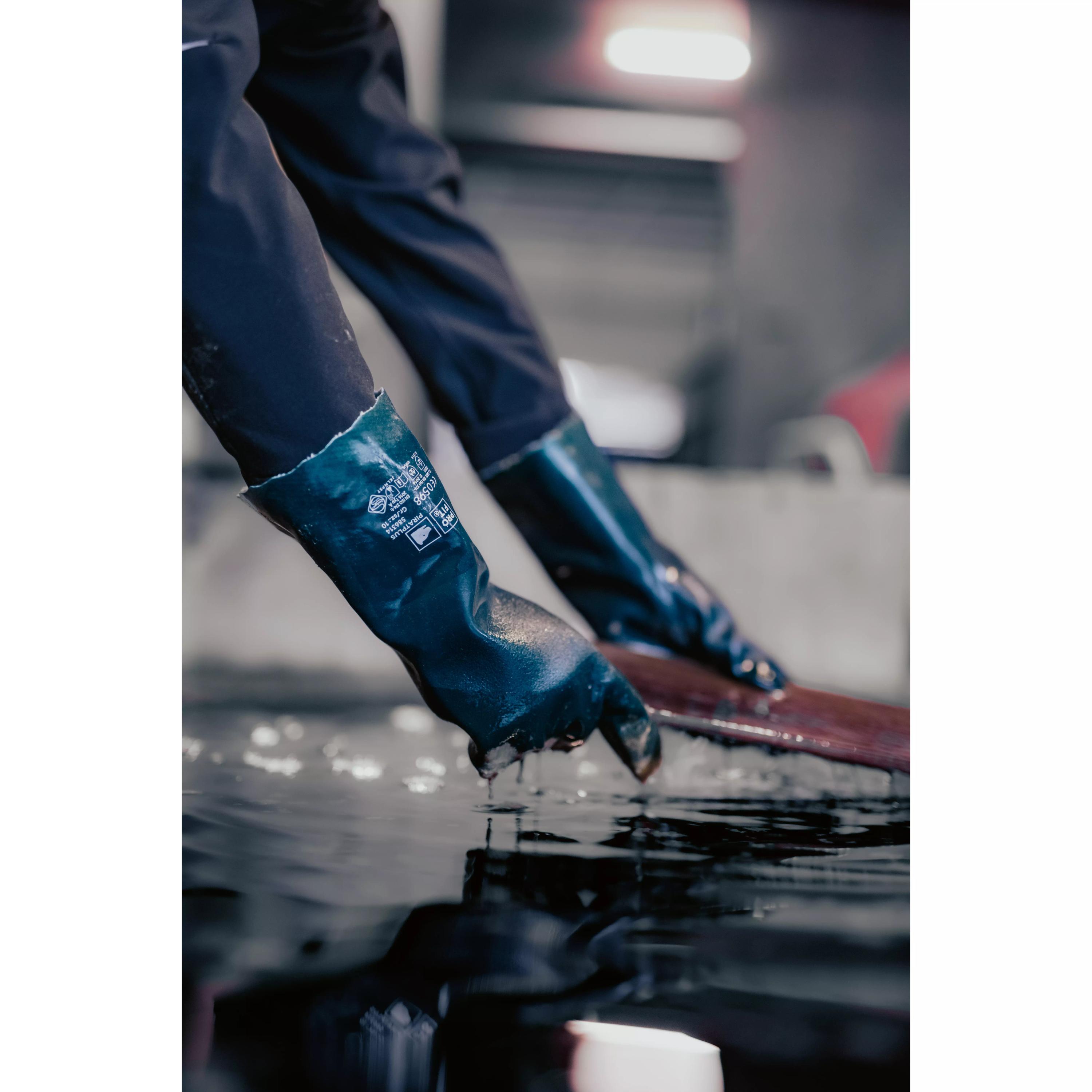 Zwei Hände tragen den Chemikalienschutzhandschuh Vinyl 40 mit angerauter Oberfläche und übertragen dunkle Flüssigkeit mithilfe eines Metalltrichters.