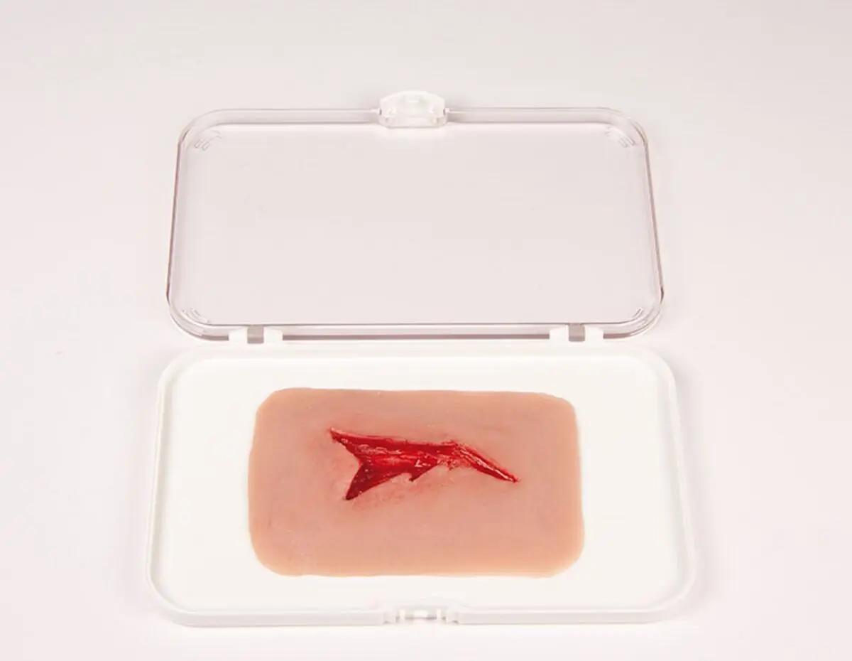 Eine Erler-Zimmer Woundmoulage Risswunde liegt in einer weißen Kunststoffschale, das Modell zeigt einen unregelmäßigen, blutenden Riss in hellrosa Schaumstoff.